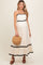 woman wearing a cream maternity maxi dress with black ruffled trim and holding a straw handbag