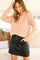 woman wearing a blush pink quarter-zip sweater and a black leather mini skirt, posing with one hand in her pocket