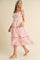 woman wearing a sleeveless pink and white floral tiered maxi dress with ruffled details and a headscarf