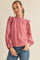 woman wearing a pink textured blouse with ruffled sleeves and a high neckline, paired with blue jeans