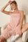 woman sitting in a chair wearing a pink fringe mini dress and white sneakers, smiling with one hand on her head