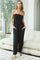 woman wearing a black strapless jumpsuit with pockets and gathered detailing, standing in a cozy interior setting