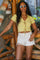 woman wearing a light yellow ribbed crop top with tie details and white high-waisted shorts, posing outdoors