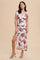 woman wearing a white floral maxi dress with a deep v-neck and side slit, standing against a beige background