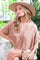 woman wearing a taupe short sleeve blouse with a v-neckline and a wide-brimmed hat, seated with a clutch bag
