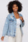 smiling woman with curly hair wearing a distressed light wash denim jacket over a white top