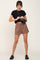 woman wearing black crop top, brown drawstring shorts, and black crossbody bag against a white background