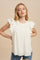 Woman wearing a white sleeveless blouse with eyelet ruffle shoulders and pleated bodice against a beige background