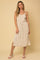 woman wearing a beige linen midi dress with spaghetti straps and a tie waist against a tan background