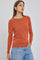 woman wearing a long-sleeved burnt orange crewneck sweater and light wash denim jeans