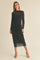 woman wearing a black long sleeve midi dress with ruched detailing and sheer sleeves, standing elegantly against a neutral background