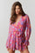 woman wearing a vibrant pink and purple floral wrap dress with long sleeves and a tie waist detail