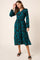woman wearing a teal long sleeve wrap dress with black floral print and a flowing midi skirt, styled with black slide sandals