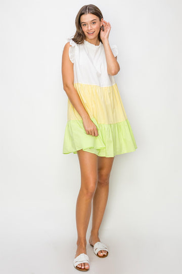 woman wearing a color-blocked sleeveless dress with white, yellow, and green tiers, styled with ruffled sleeves and sandals