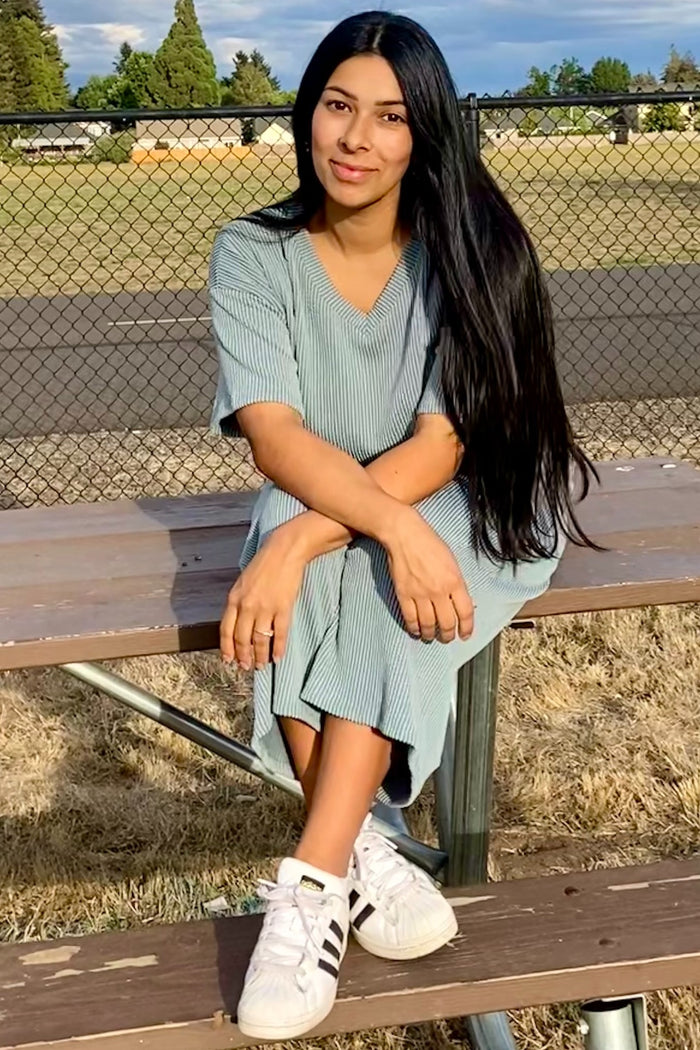 woman wearing a green and white striped midi dress and white sneakers, sitting on a bench outdoors