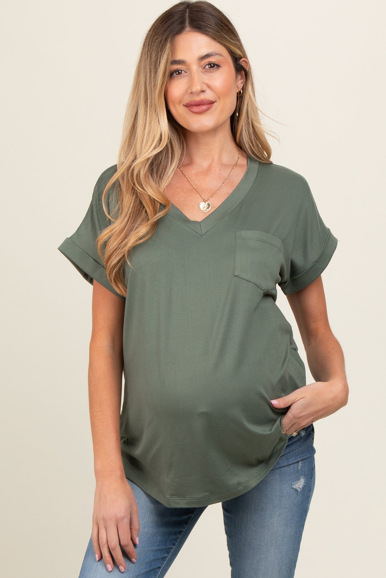 woman wearing a dark green maternity top with a pocket and rolled sleeves, showing her baby bump and paired with jeans