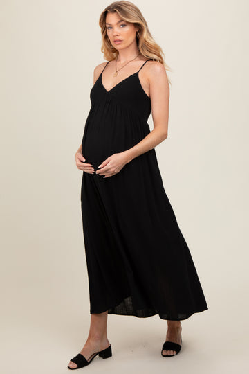 woman wearing a black maternity maxi dress, holding her baby bump while standing sideways