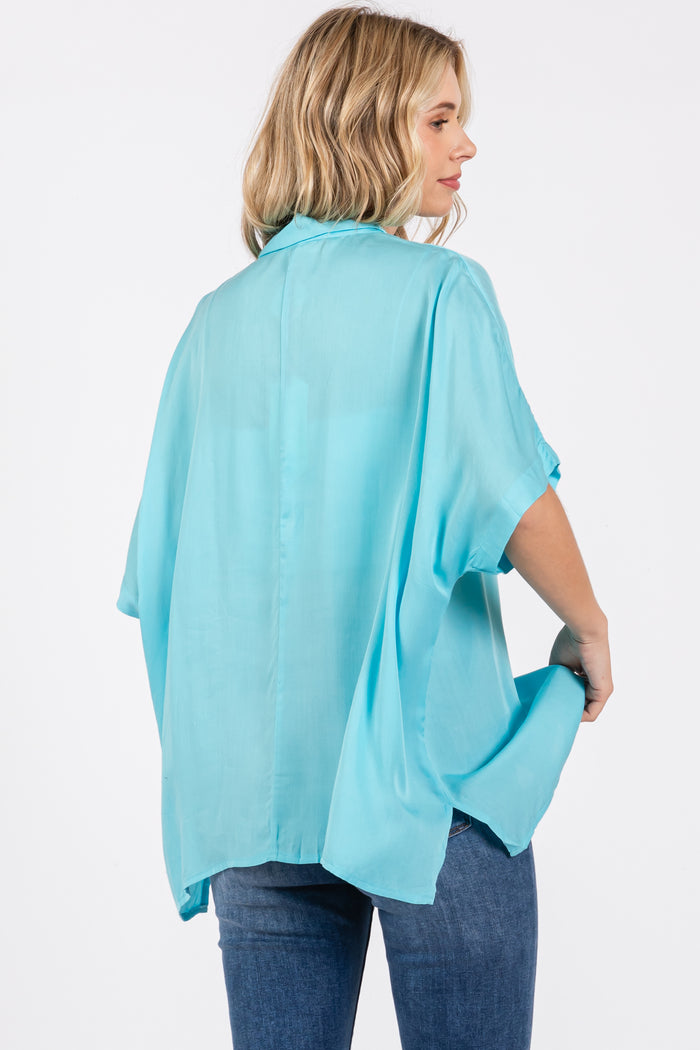 woman wearing a light blue flowy kimono-style top with short sleeves and a back pleat