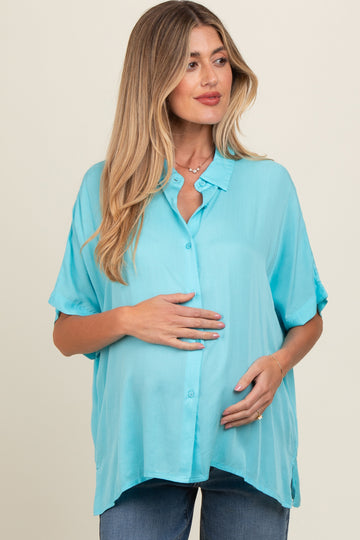 woman wearing a turquoise maternity shirt with short sleeves and button details, holding her baby bump