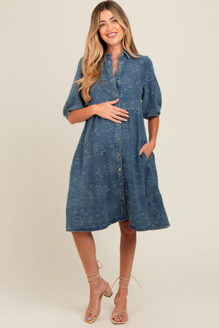 woman wearing a denim blue maternity dress with short puff sleeves, button front, and side pockets, showcasing her baby bump