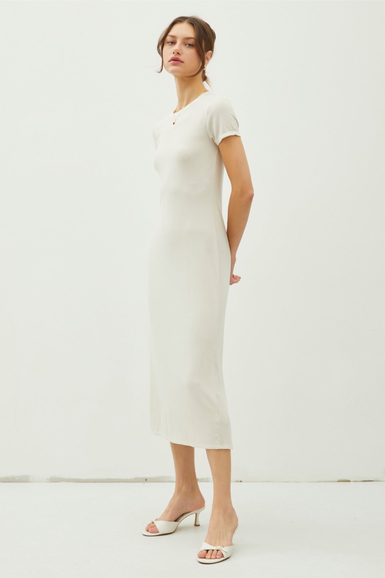 woman wearing a light beige short sleeve midi dress and white heeled mules