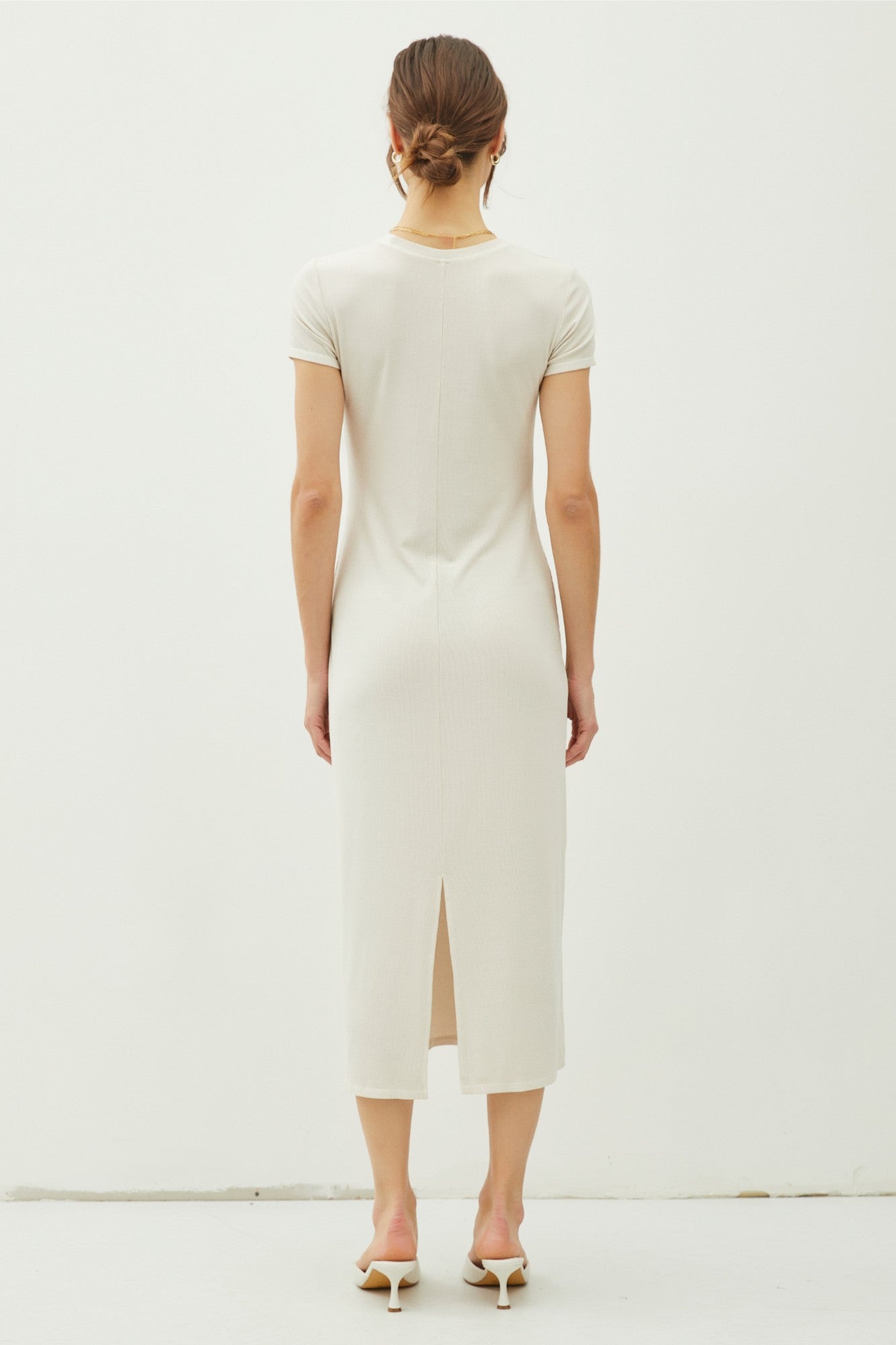 woman wearing a fitted cream-colored midi dress with short sleeves and a back slit