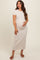 woman wearing a light beige short sleeve maternity dress and holding her baby bump