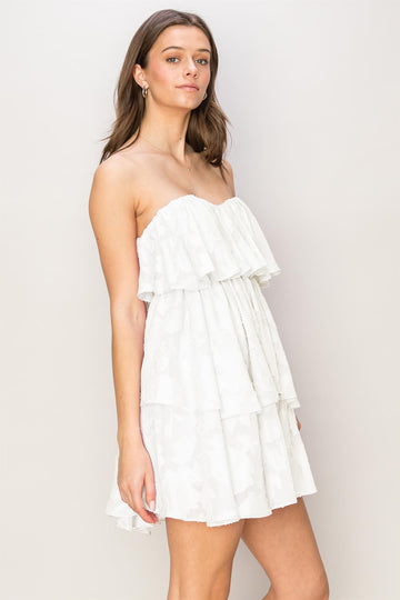 woman wearing a white strapless tiered mini dress with ruffle details