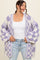 woman wearing a purple and white checkered oversized cardigan with bell sleeves and a white tank top underneath