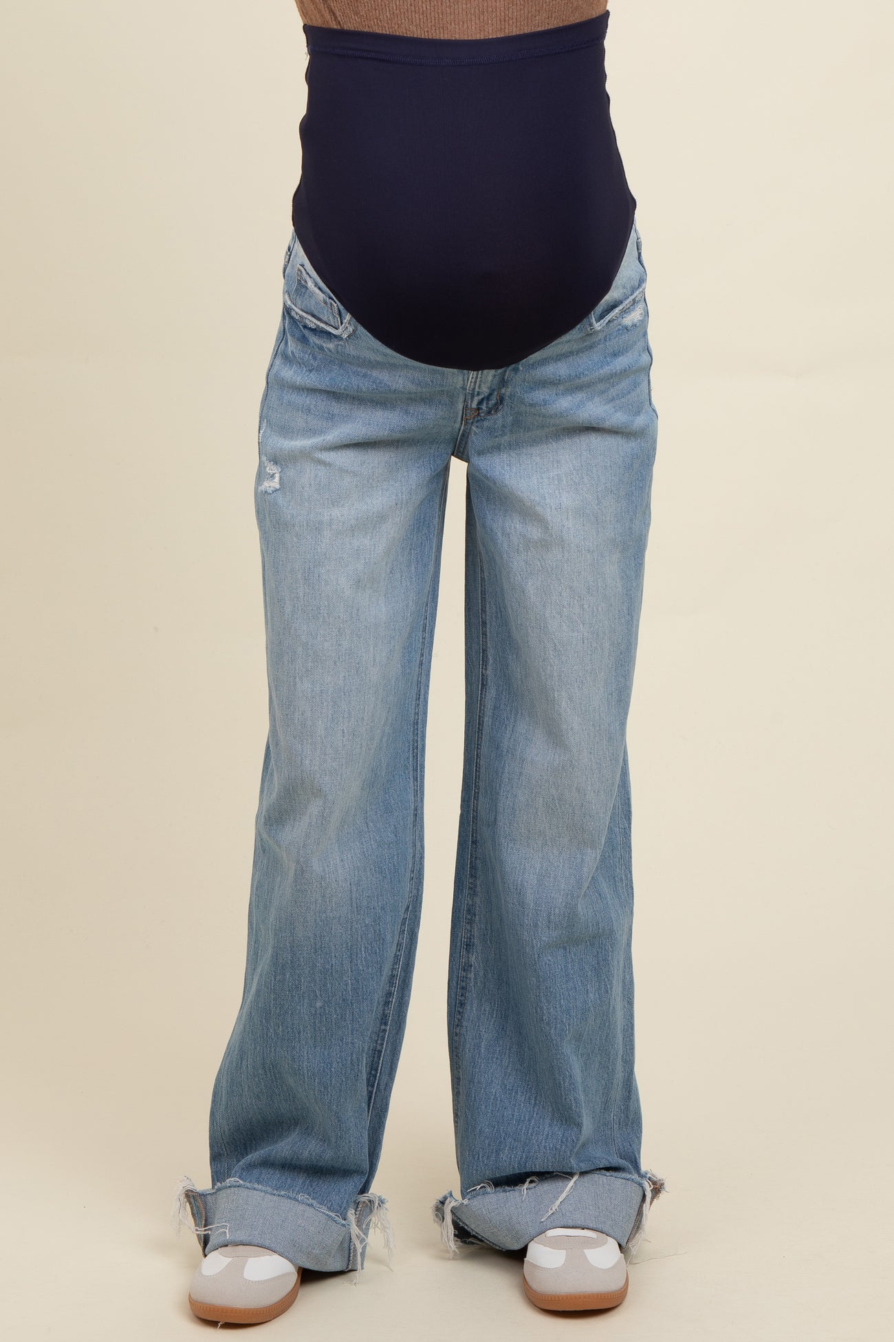 woman wearing a pair of light blue maternity jeans with a navy blue belly band and frayed hem details, baby bump visible