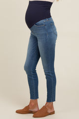 woman wearing a pair of blue maternity skinny jeans with a navy belly panel and frayed hem, showcasing a visible baby bump