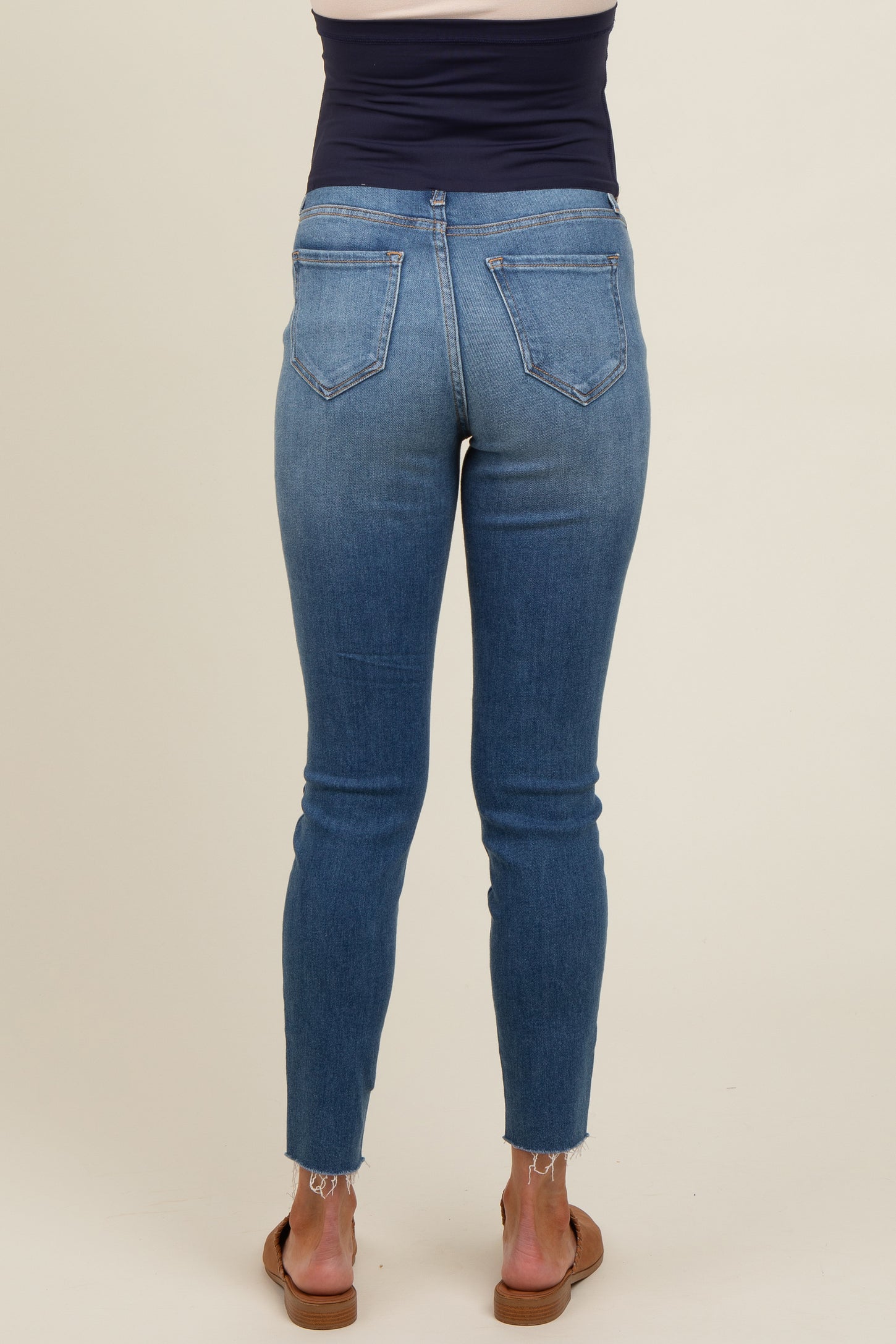 woman wearing dark blue maternity jeans with a skinny fit and frayed hem, showing the back view