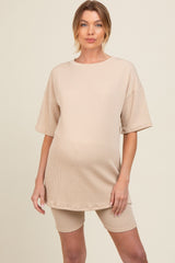 woman wearing a beige maternity oversized t-shirt dress with matching bike shorts, showing a visible baby bump