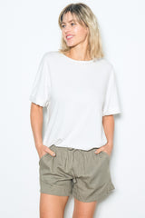 woman wearing a white oversized t-shirt and olive green drawstring shorts, smiling and posing against a white background
