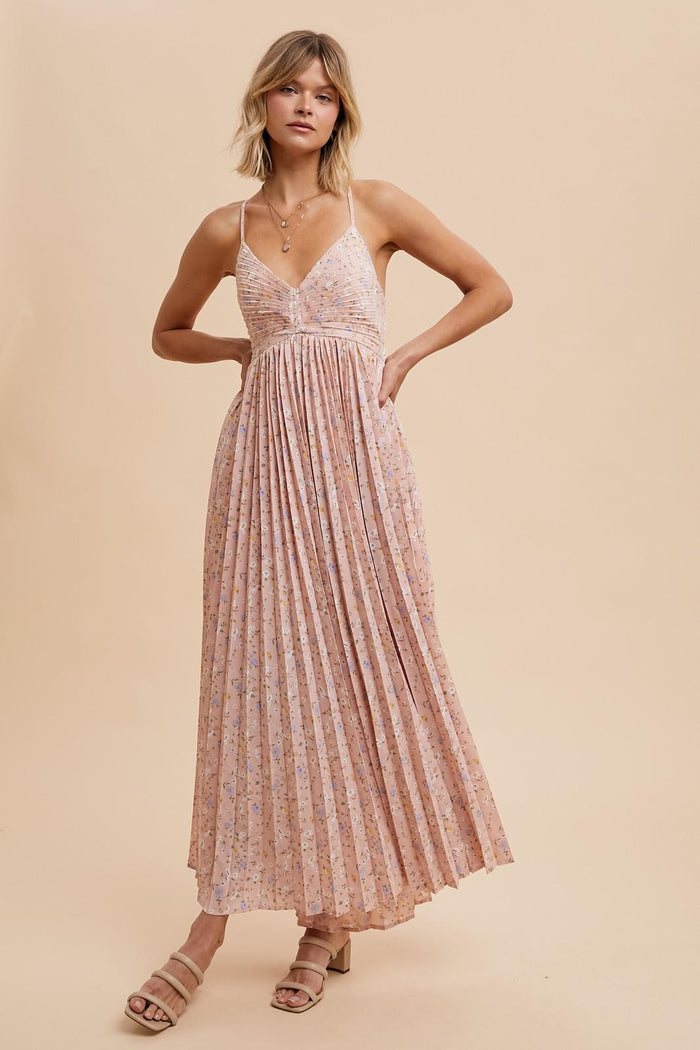 woman wearing a floral maxi dress with pleated details and thin straps, standing against a neutral background