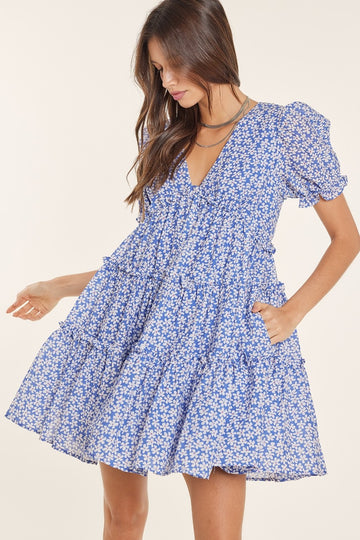 woman wearing a blue floral puff sleeve mini dress with a tiered skirt and a deep v-neckline