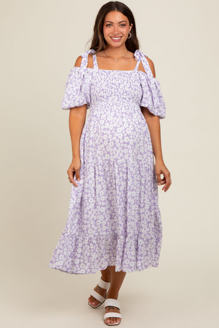 woman wearing a lilac floral cold shoulder maternity dress with puff sleeves and a tiered skirt