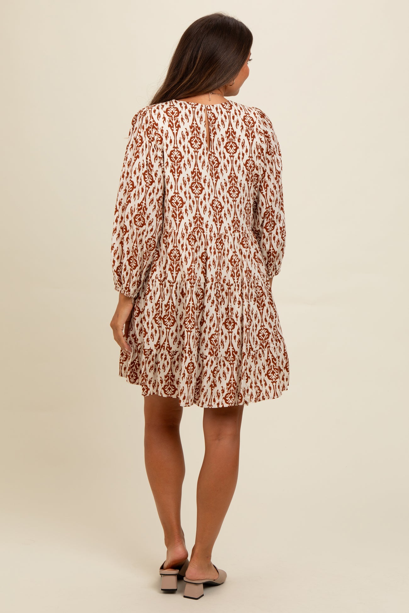 woman wearing a cream and rust-colored patterned maternity dress with long sleeves and a flared skirt, showing her back