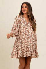 woman wearing a cream and rust printed maternity dress with a flowy silhouette and long sleeves