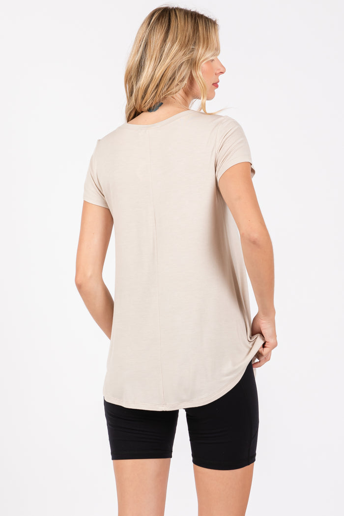 woman wearing a beige short sleeve top with a relaxed fit and longer back, paired with black shorts