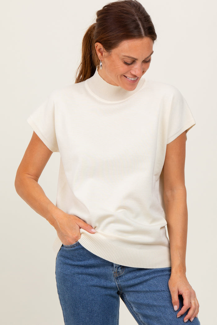 woman wearing a cream short sleeve mock neck sweater and blue jeans, smiling while looking down