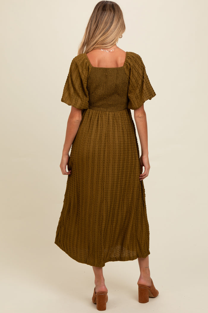 woman wearing a dark olive green maternity dress with a smocked bodice and short flutter sleeves, showing a pregnant belly