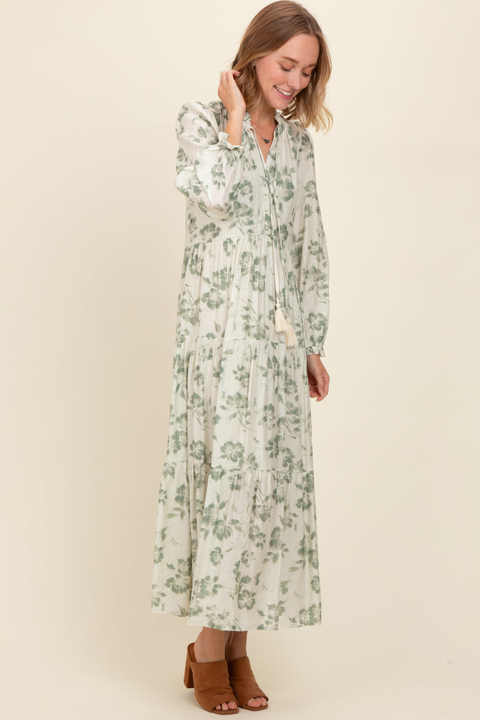 woman wearing a long sleeve green floral maxi dress with tiered detailing and a tassel tie neckline