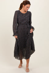 woman wearing a black floral midi dress with long sleeves and a belted waist, standing and looking down