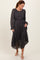 woman wearing a black floral midi dress with long sleeves and a belted waist, standing and looking down