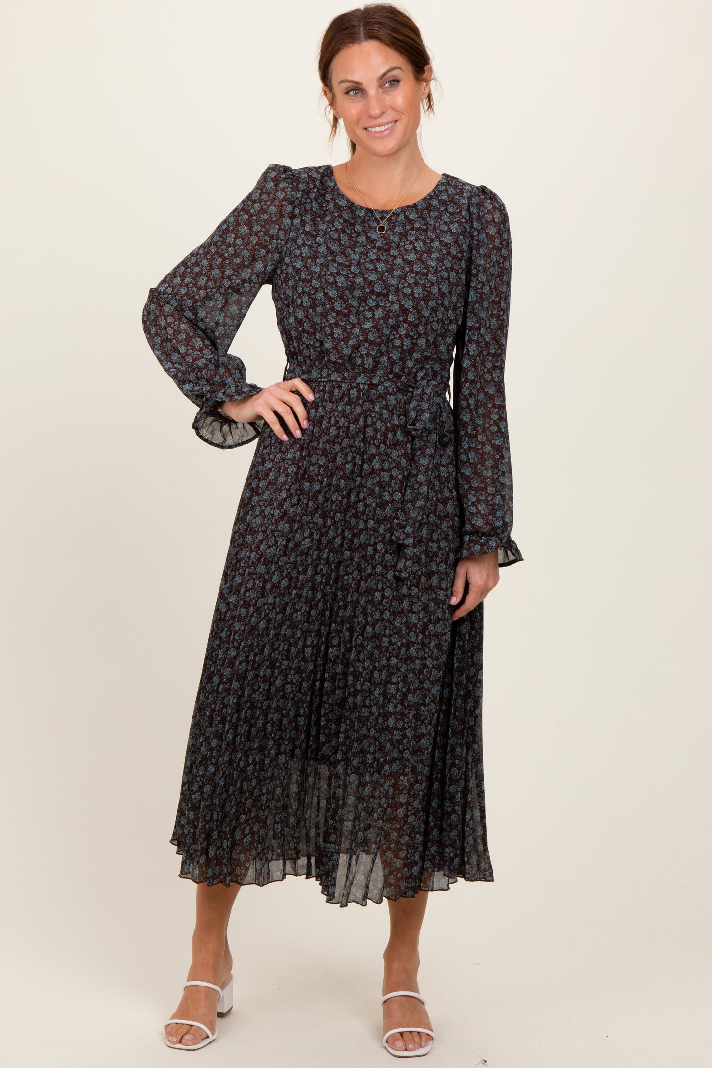 woman wearing a dark floral midi dress with long sleeves and ruffled cuffs, smiling at the camera