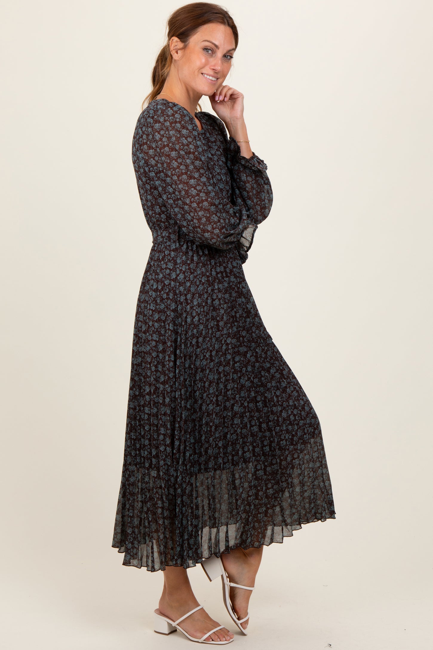 woman wearing a black floral maxi dress with long sleeves and a tiered skirt, smiling and posing to the side