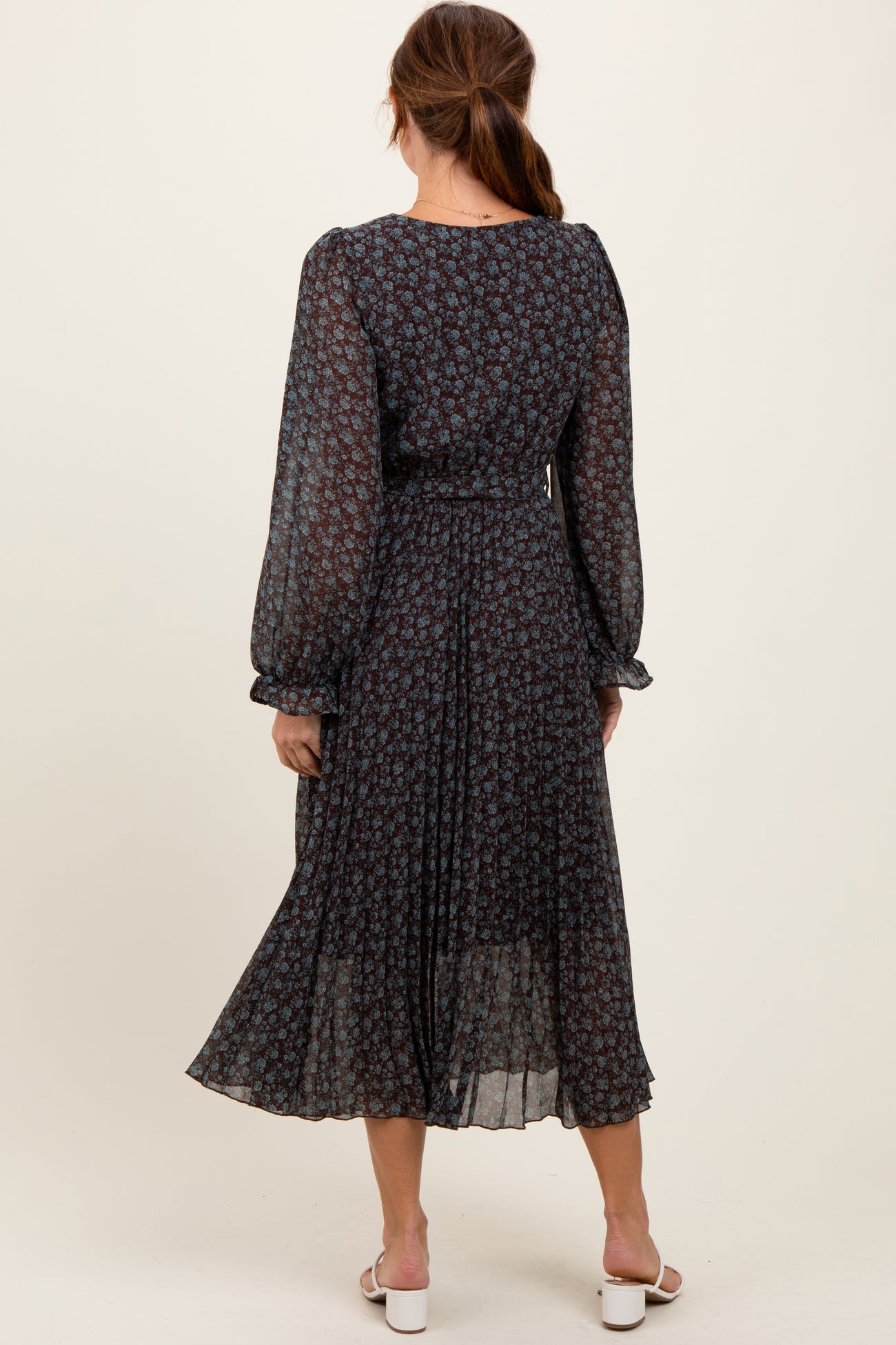 woman wearing a dark floral long sleeve midi dress with a pleated skirt and a cinched waist, viewed from the back