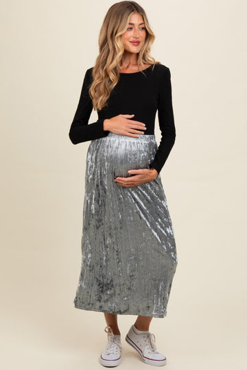 woman wearing a black long sleeve maternity top and a silver crushed velvet maxi skirt, holding her baby bump