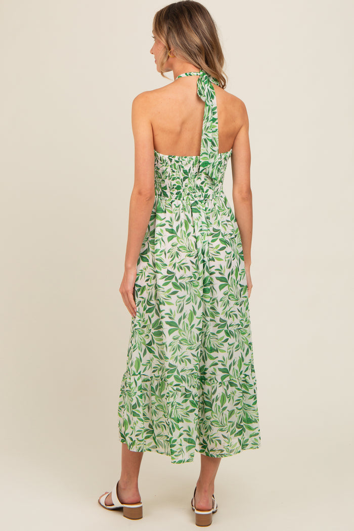 woman wearing a backless green leaf print maxi dress with a halter neck and smocked bodice